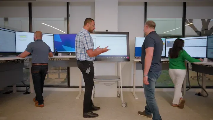 Four SLB engineers collaborating at Performance Live center with large display screens by Motion Giraffx