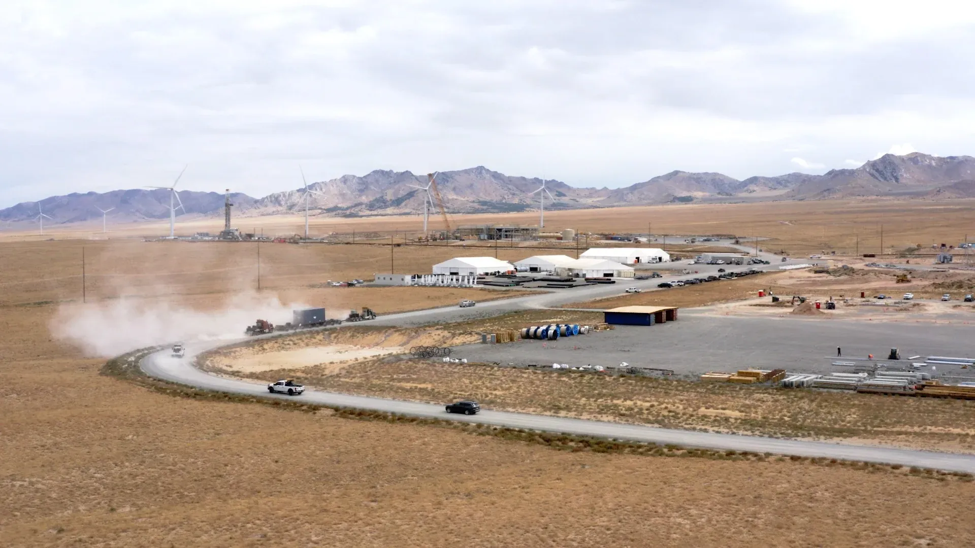 Aerial establishing shot of Fervo's Cape Station drill pad with a service truck kicking up dust against the high-desert mountains, from the roadshow film by Motion Giraffx.