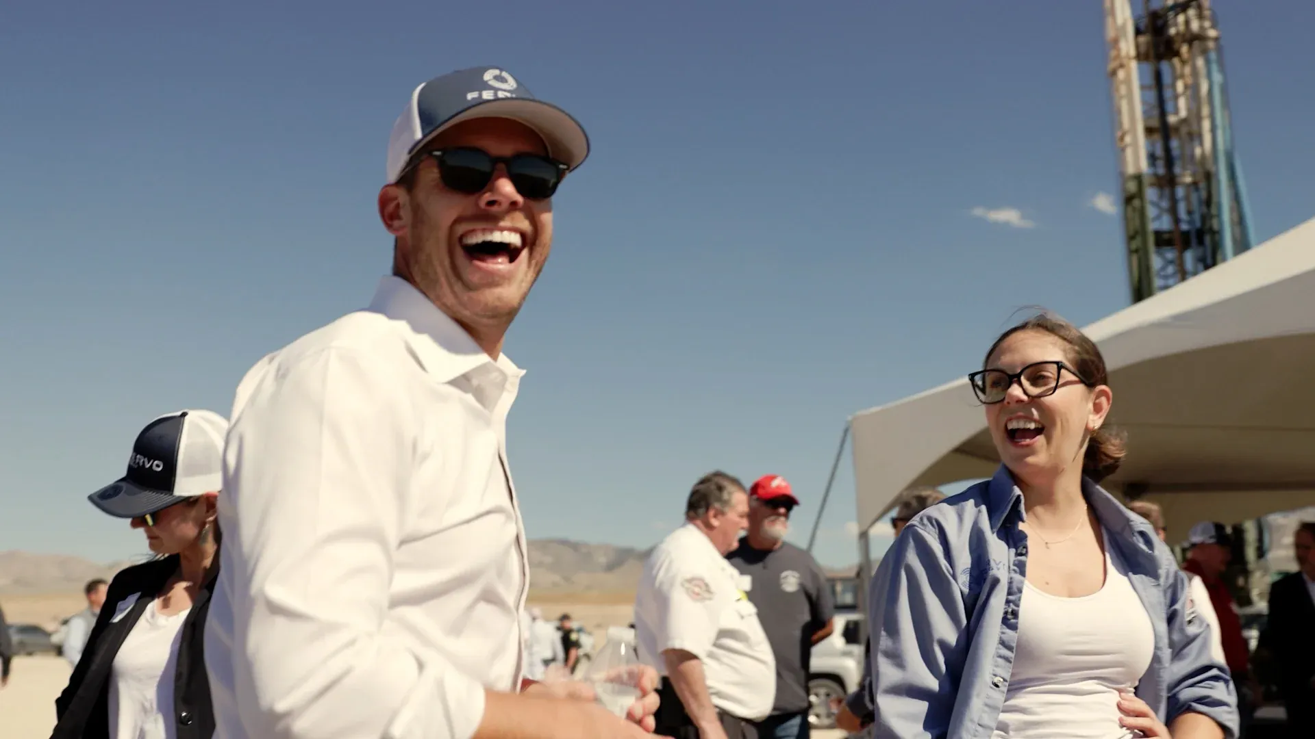Fervo executive laughing with a colleague on a sunlit drilling pad with a rig in the background, from the roadshow film by Motion Giraffx.