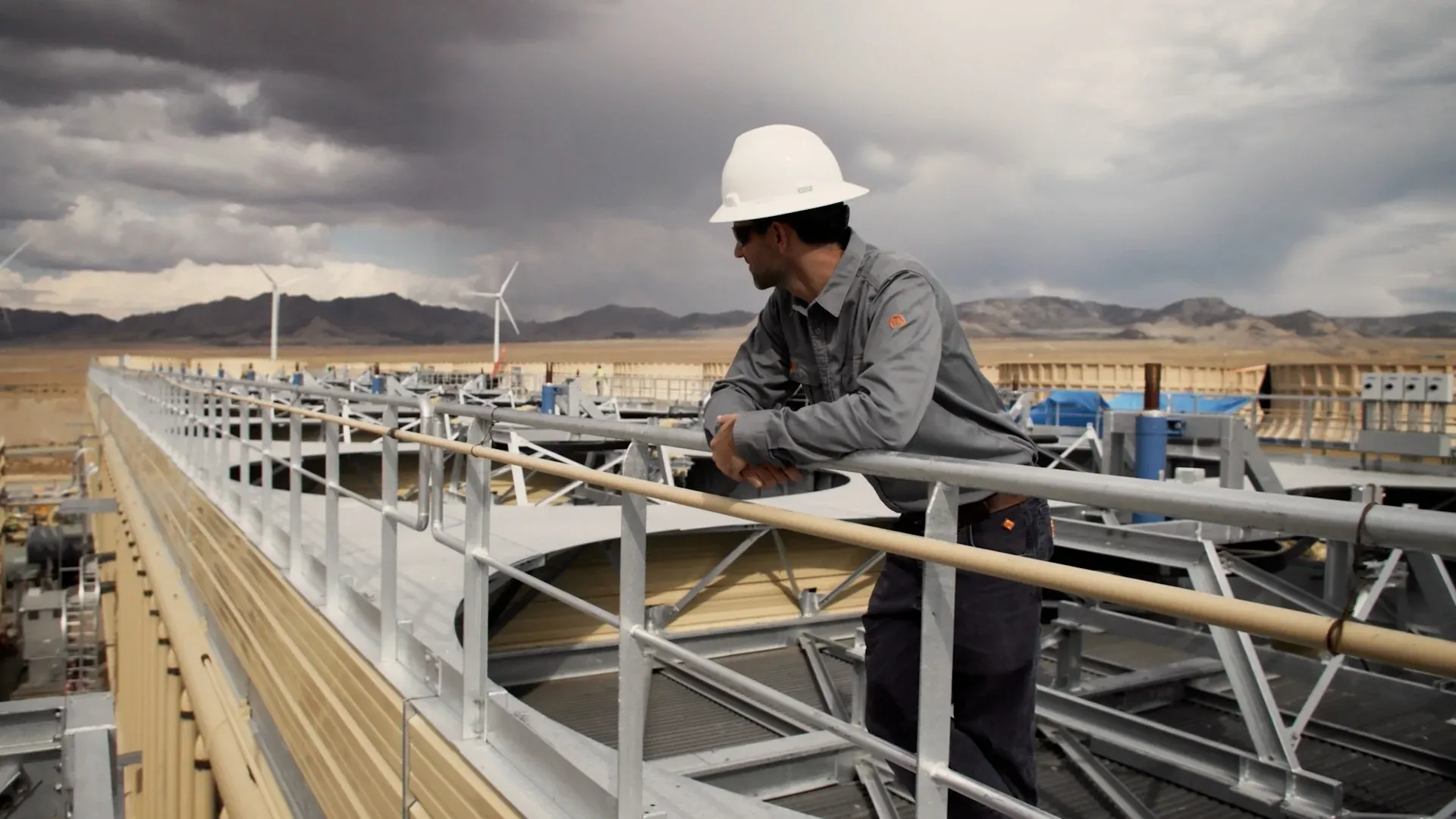 Hard-hatted Fervo operator overlooking the Cape Station cooling array under stormlight, captured by Motion Giraffx.