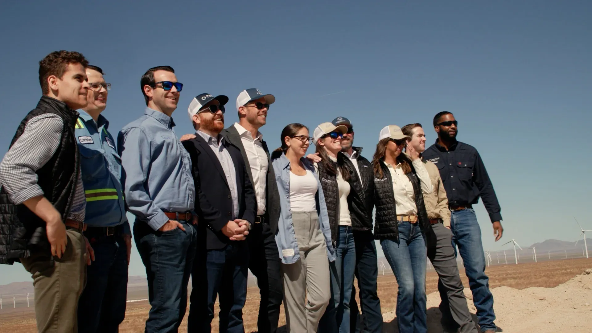 Group portrait of the Fervo Energy team at the Cape Station wind farm under a blue sky, from the roadshow film by Motion Giraffx.
