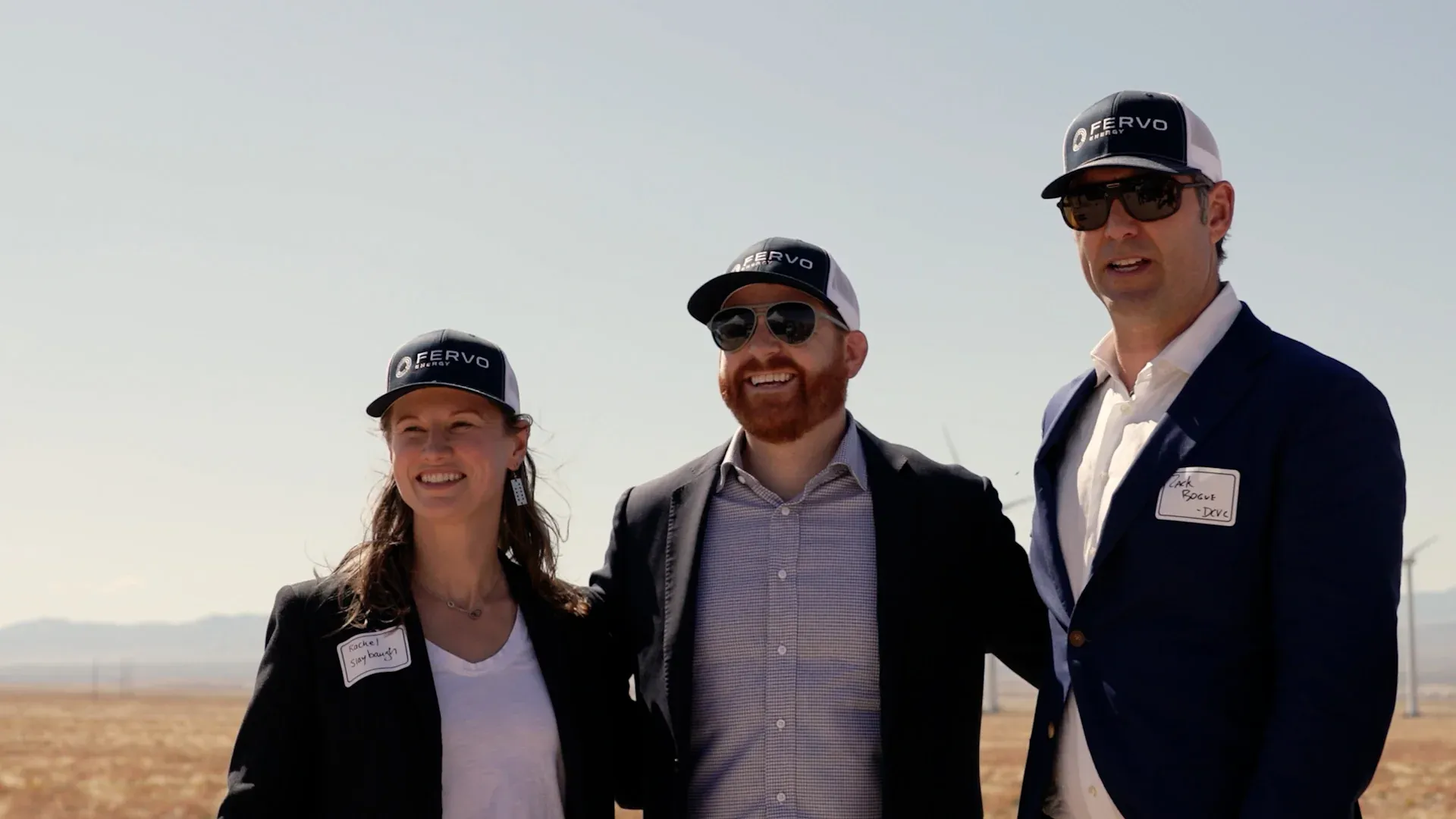 Fervo Energy team members posed at a wind farm site in branded caps, from the roadshow film by Motion Giraffx.