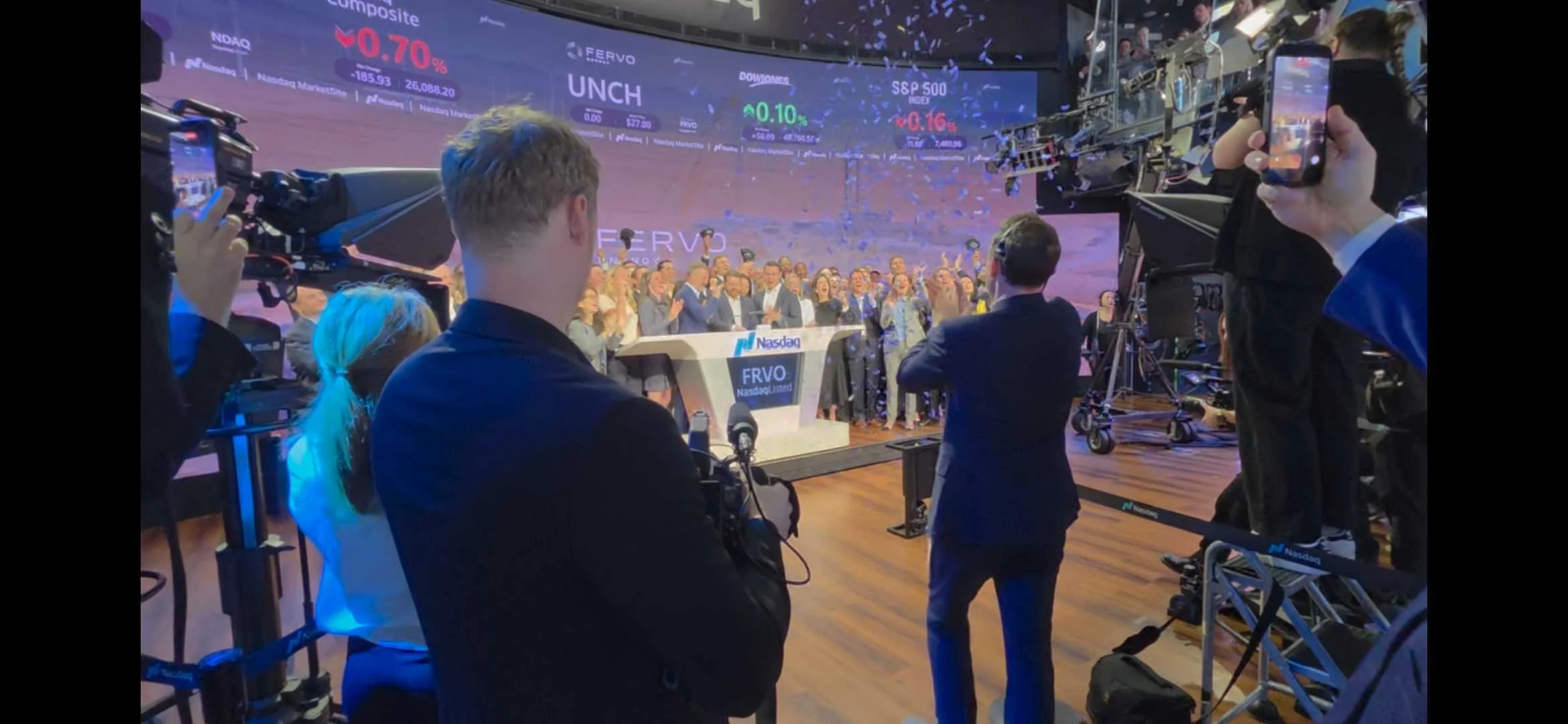 Fervo Energy executives raising their arms in celebration on the Nasdaq MarketSite podium with confetti falling and the FRVO ticker visible on the video wall behind them, captured by Motion Giraffx at the May 13, 2026 opening bell ceremony.
